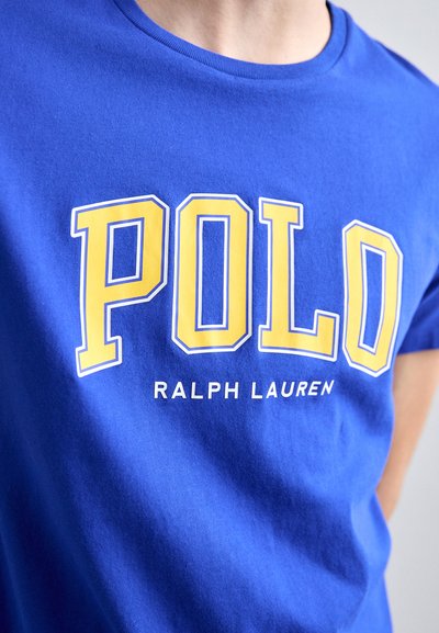 Camiseta de algodón azul con gran texto amarillo "POLO" contorneado en blanco y el texto más pequeño "RALPH LAUREN" debajo, con cuello redondo.