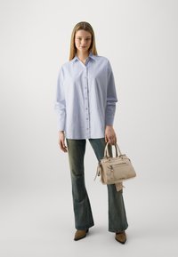 Lichtblauwe gestreepte overhemd met lange mouwen, gecombineerd met donkere groene flared jeans en een beige handtas met ritsen en accenten.