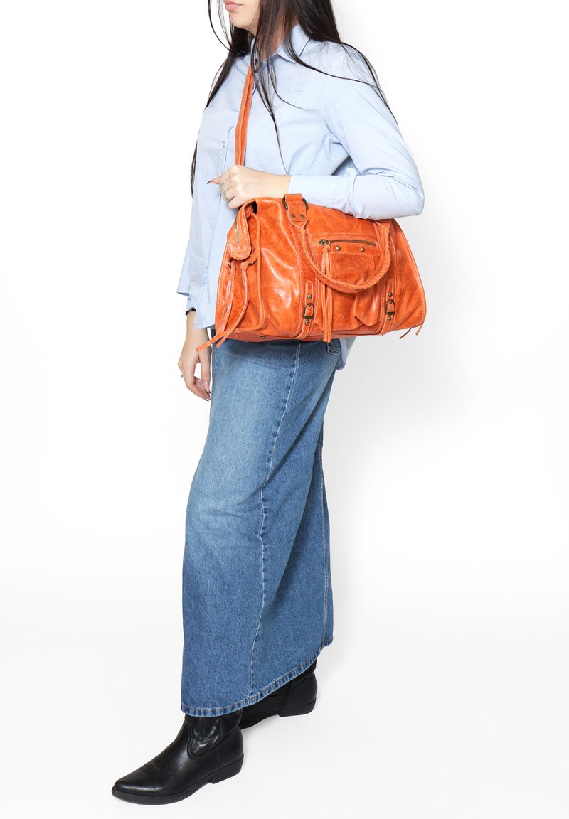 Sac à main en cuir orange avec plusieurs compartiments, texture lisse et bandoulière réglable, porté sur une chemise bleue et une jupe en denim.