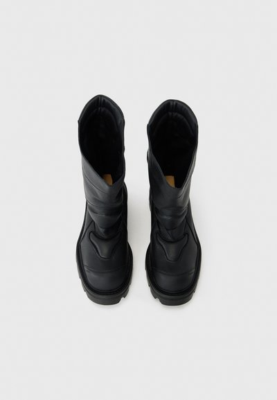 Schwarze Lederstiefel mit strukturiertem Finish, ausgestattet mit einem hohen Design, Nähdetails und einer abgerundeten Spitze. Weiches Innenfutter ist sichtbar.