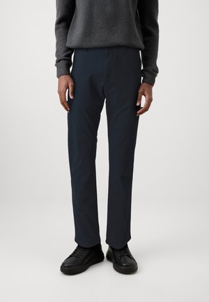 Marineblaue Hose mit schmalem Schnitt, aus einem leichten Stoff gefertigt. Besitzt ein gerades Bein-Design und seitliche Taschen, kombiniert mit schwarzen Sneakers.