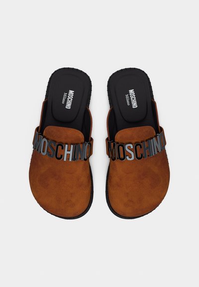 Sandales marron à enfiler avec semelles noires, ornées de grandes lettres noires en relief formant le mot "MOSCHINO" sur les brides supérieures.