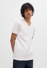 White short-sleeve V-neck t-shirt made of smooth, lightweight fabric, paired with dark denim jeans. Simple design, no visible patterns.