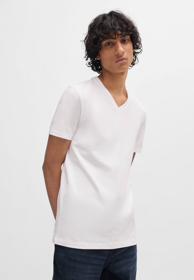 White short-sleeve V-neck t-shirt made of smooth, lightweight fabric, paired with dark denim jeans. Simple design, no visible patterns.