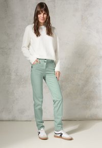 Pantalones verde menta de corte ajustado con bolsillos frontales, combinados con un suave suéter blanco. El modelo lleva zapatillas blancas con detalles en negro.