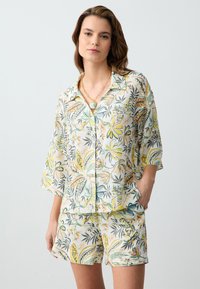Ensemble de loungewear floral en tissu léger ; chemise à manches courtes et shorts avec des motifs de plantes verts, jaunes et oranges ; coupe décontractée.