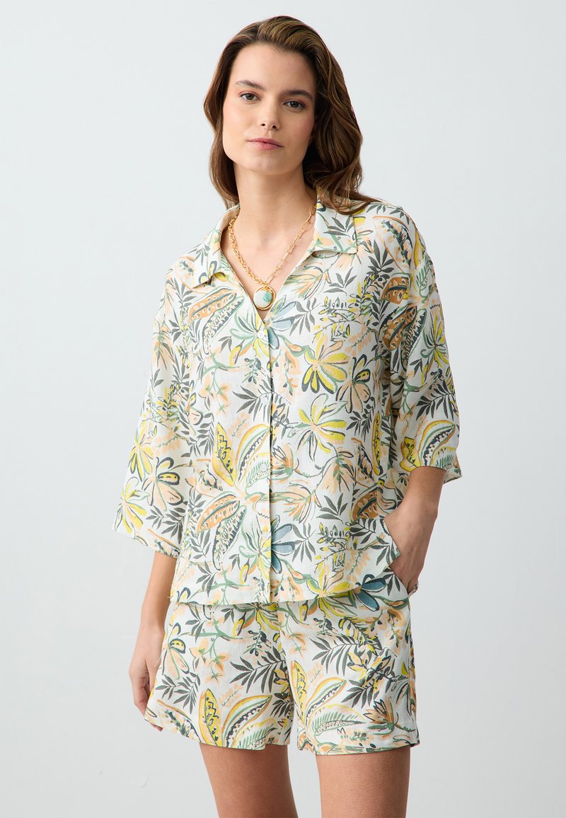 Ensemble de loungewear floral en tissu léger ; chemise à manches courtes et shorts avec des motifs de plantes verts, jaunes et oranges ; coupe décontractée.