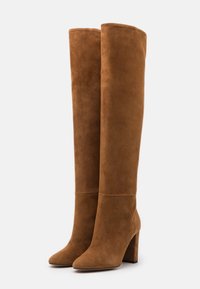 Brune ruskindsstøvler til knæet med firkantet tå og blokhæle, der har en glat tekstur og sømløs design uden synligt hardware.