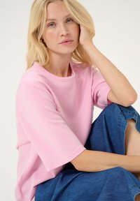 Svetlo roza kratka majica s kratkimi rokavi in okroglo ovratnikom ter mehko teksturo, v kombinaciji z modrimi kavbojkami, ki imajo rahlo raztrgano rob.