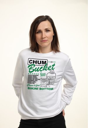 Frau trägt weißen Sweatshirt mit grünen und schwarzen Texten und Illustrationen, die das Restaurant "Chum Bucket" aus Bikini Bottom bewerben.