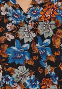 Tissu à imprimé floral avec de grandes fleurs bleues, vertes et orange sur fond noir, avec une surface texturée et un col en V profond.