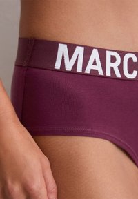 Burgunderfarbene Baumwoll-Hipster-Unterwäsche mit einem breiten, weißen, elastischen Bund, auf dem das Wort "MAR" groß hervorgehoben ist. Weiche Textur, taillierter Schnitt.