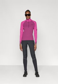 Aangesloten sporttop met lange mouwen in felroze met een halve rits, gecombineerd met donkergrijze leggings met reflecterende accenten. Zwarte schoenen.