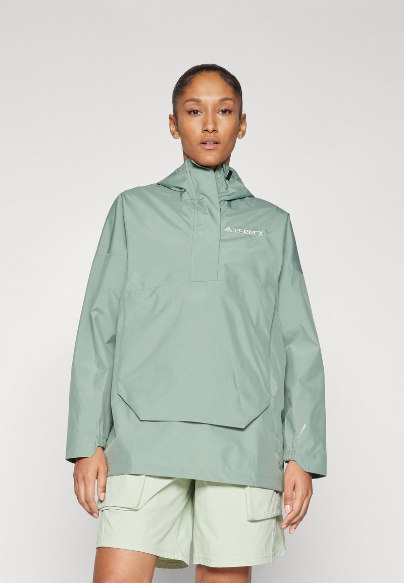 Lichtgroene waterdichte jas met een halfritsontwerp, hoge kraag en grote voorzak. Gecombineerd met lichtgroene cargoshorts.