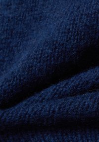 Gros plan sur un tissu tricoté douillet de couleur bleu foncé, avec des fibres visibles et un tissage texturé, montrant des plis et des ombres.
