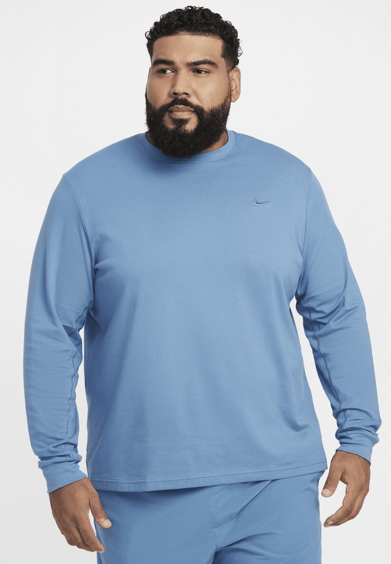Niebieska koszulka Nike z długim rękawem, wykonana z gładkiego, przewiewnego materiału; posiada małe czarne logo na piersi oraz okrągły dekolt.