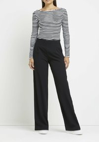 Randig långärmad topp i vitt och svart, kombinerad med högmidjade svarta vidbyxor. Outfiten har en enkel och raffinerad design.