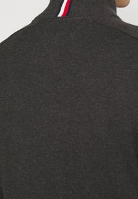 Ciemnoszary sweter z golfem o prążkowanej fakturze. Posiada kołnierz w paski w kolorach czerwonym, białym i niebieskim. Czysty, dopasowany krój.