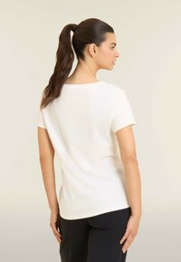 Camiseta blanca de manga corta hecha de tela suave, con un escote redondo y un ajuste ligeramente holgado, exhibida en un modelo con pantalones negros.