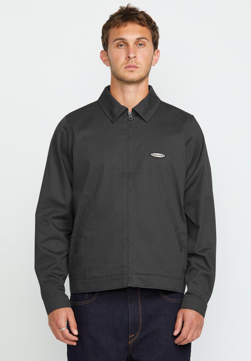Grijze zip-up jas met een puntkraag, twee voorzakken en een klein merklogo op de borst. Zachte stof met een gladde textuur.