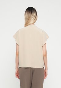 Top beige a maniche corte con scollatura rotonda, tessuto liscio e zip al centro sul retro. Abbinato a pantaloni marroni, casual e larghi.