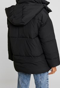 Svart puffjacka med huva, med en quiltad yta och lös passform. Jackan har en mjuk yta och elastiska ärmslut.