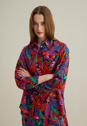 Camisa de botones colorida con un vibrante patrón floral en rojo, verde y púrpura, con un corte relajado y mangas largas.