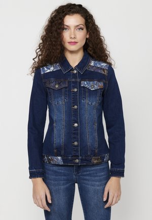Dark blue denim jacket featuring contrasting patterned fabric on the shoulders and waistband, with metal buttons and two front pockets.