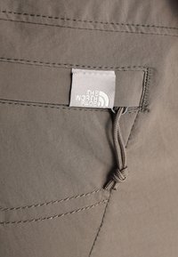 Harmaa kangashousut, joissa on näkyvä pieni tasku. The North Face -logotunnus kiinnitetty taskuun; sisältää ompeleita ja vetoketjun.