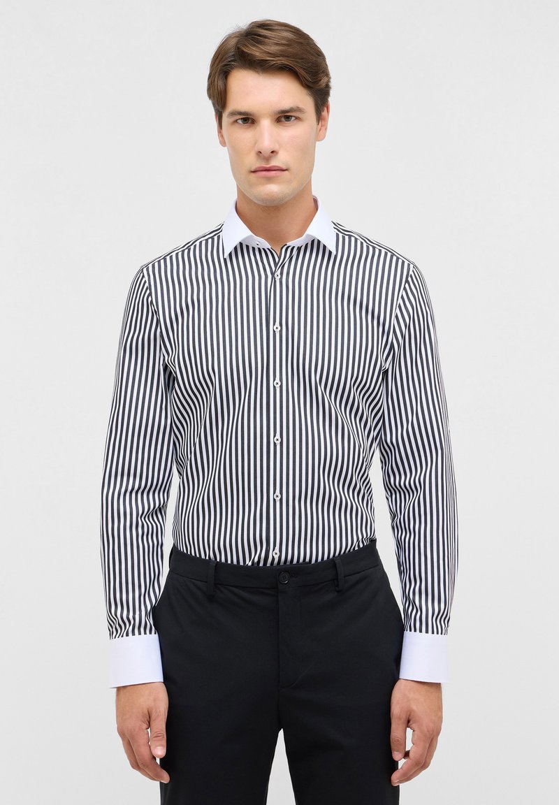 Een button-up shirt met verticale zwart-witte strepen, een contrasterende witte kraag en lange mouwen. Draagt het met zwarte broek.