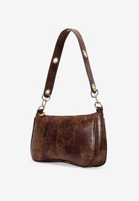 Bolso de mano de cuero marrón con una forma ligeramente curvada, terminado con una superficie texturizada. Presenta un asa con accesorios en tono dorado.