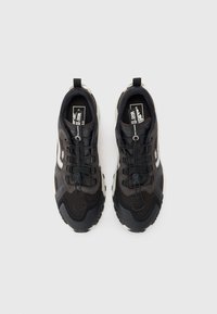 Black athletic shoes featuring a mix of textured mesh and synthetic materials, with elastic laces, and a white midsole.