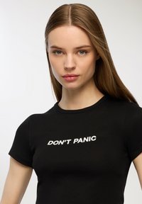 Maglietta nera in cotone con design aderente, scollatura rotonda e maniche corte, con la scritta bianca "DON'T PANIC" sulla parte anteriore.