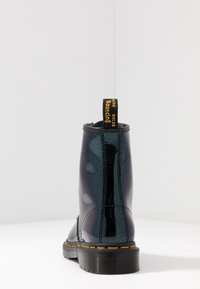 Bottine noire en cuir verni avec une finition brillante, onglet jaune "Bouncing Soles" et couture orange contrastante le long de la semelle.