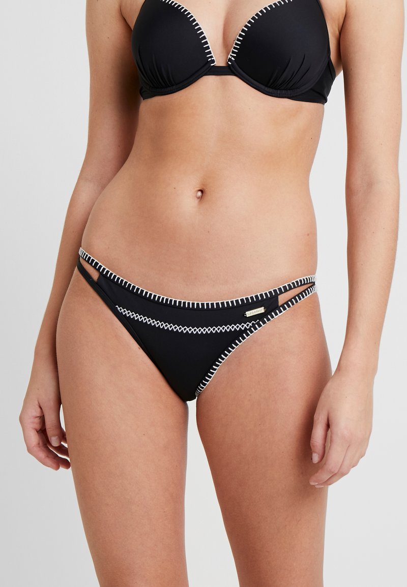Svart bikini med trekantet topp og snøre detaljer. Hvite sømmer som aksenterer og utskjæringsdetalj på bikiniunderdelen. Glatt tekstur.