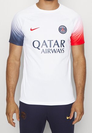 Mężczyzna ubrany w białą koszulkę piłkarską Paris Saint-Germain z logo Qatar Airways i gradientowymi, niebiesko-czerwonymi rękawami, połączoną z granatowymi spodniami.