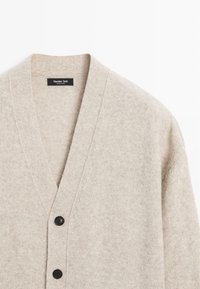 Beżowy wełniany kardigan z głębokim dekoltem w serek, z czarnymi guzikami i miękką fakturą. Metka z napisem "Massimo Dutti".