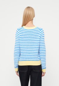 Sinivalkoraidallinen neulepaita, jossa on keltainen resorireuna helmassa ja hihoissa, valmistettu pehmeästä, pörröisestä materiaalista. Siinä on pyöreä pääntie ja pitkät hihat.