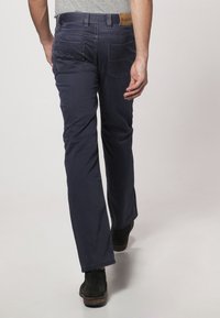 Granatowe chinosy o kroju prostych nogawek, z tylnymi kieszeniami i kontrastującym przeszyciem, zestawione z czarnymi botkami za kostkę.