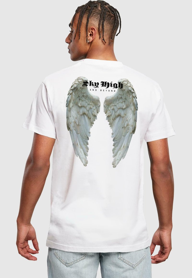 T-shirt en coton blanc avec un graphisme d'ailes d'ange en gris au dos, avec "Sky High and Beyond" imprimé au-dessus en gras noir.