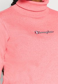 Sudadera de cuello vuelto en color rosa, hecha de tejido suave con un ribete en el cuello, que presenta un pequeño logotipo bordado de Champion en blanco y rojo en el pecho.