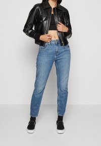 Chaqueta bomber de cuero negro con dos bolsillos frontales, combinada con jeans de talle alto en azul claro y zapatos negros tipo slip-on. Simple y casual.