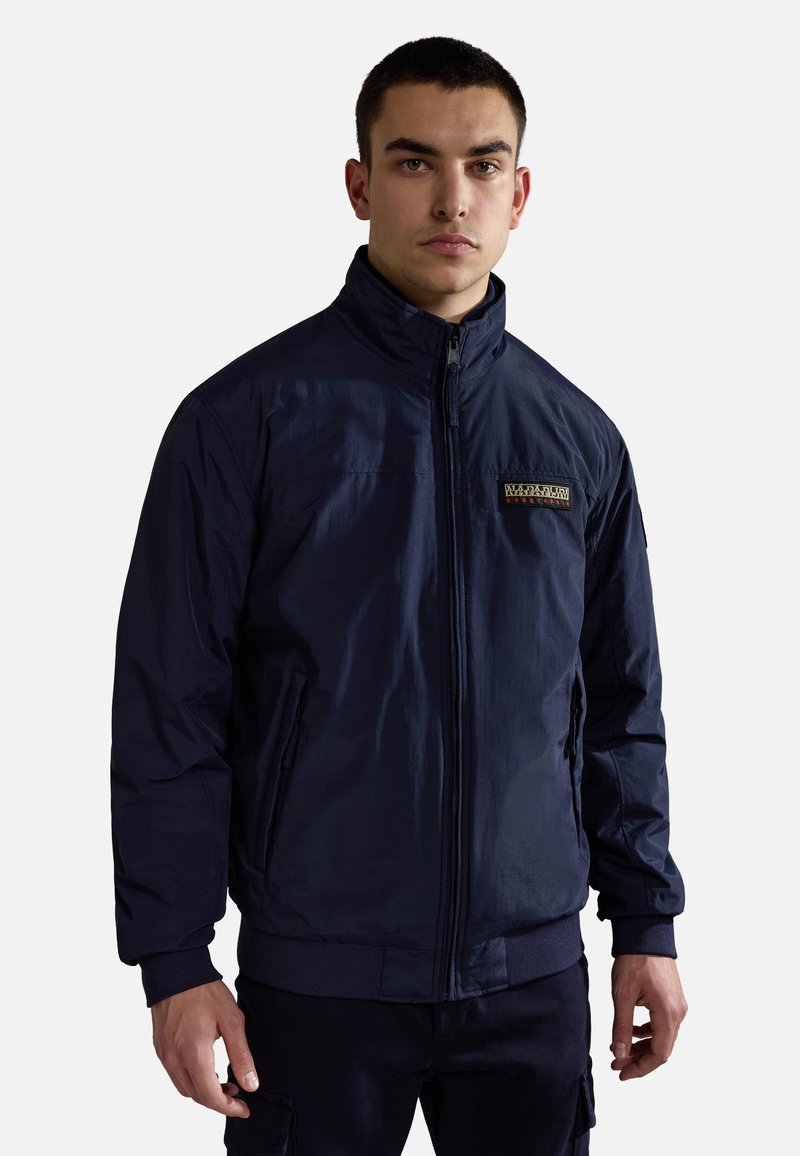 Mörkblå zip-up-jacka gjord av lättviktsmaterial, med hög krage, två sidofickor och en diskret logodetalj på bröstet.