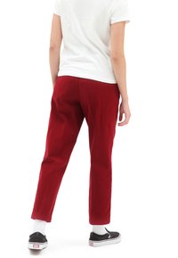 Pantaloni in corduroy rossi con vestibilità rilassata, caratterizzati da una texture liscia e un design a gamba affusolata, abbinati a sneakers nere e calzini bianchi.