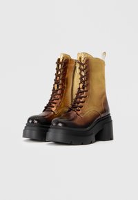 Bottines à lacets avec un dégradé métallique texturé allant du doré au bronze, dotées d'une semelle plateforme noire chunky et d'un détail de fermeture éclair sur le côté.
