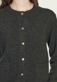 Ciemnozielony wełniany kardigan z okrągłym dekoltem, z sześcioma metalowymi guzikami z przodu i dwoma bocznymi kieszeniami. Teksturowana dzianina.