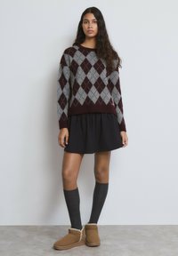 Suéter color rojo granate y gris con patrón de rombos y puños acanalados, combinado con una falda negra plisada, calcetas grises hasta la rodilla y botines color canela con borde de piel.