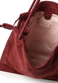 Rode suède handtas met leren accenten, voorzien van een ruim interieur bekleed met beige stof en een merklabel aan de binnenzijde.