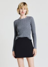 Maglione grigio a trecce con scollatura tonda, abbinato a una gonna nera aderente. Il maglione presenta dettagli testurizzati e maniche lunghe.