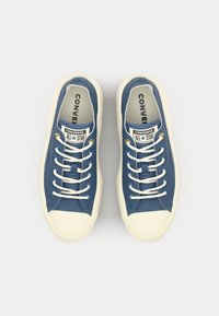 Baskets en toile bleue avec des bouts et semelles en caoutchouc blanc, dotées de lacets blancs, d'œillets dorés et de la marque 'Converse All Star' sur la languette.